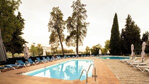 Una piscina amb gandules i ombrelles, envoltada d'arbres.