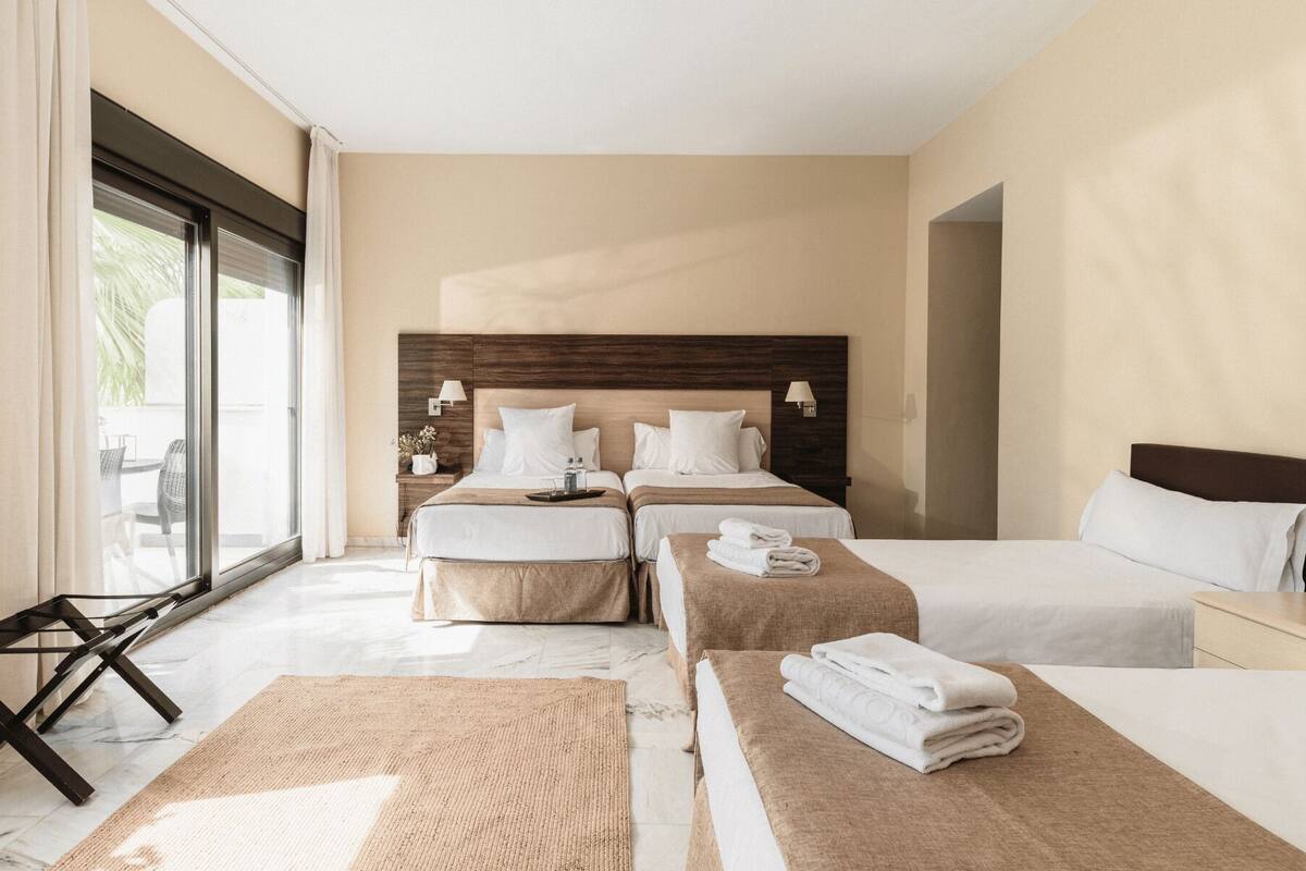Habitación de hotel con dos camas, una zona de estar con una mesa y vistas a través de un ventanal grande.