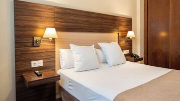 A hotel room with a wooden headboard, two bedside lamps, a bedside phone, and a bed with white bedding.
