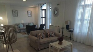 Un saló modern amb un sofà, una taula de centre i una làmpada de terra. Hi ha una porta que condueix a una altra habitació i una finestra amb cortines.