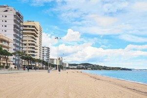 Una playa con una hilera de edificios de varios pisos, cielo despejado y mar tranquilo.