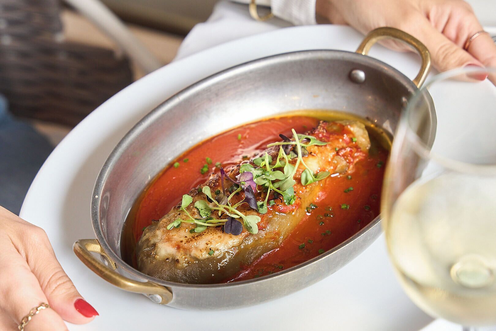 A dish with a red sauce, garnished with greens, served in a metal pan.