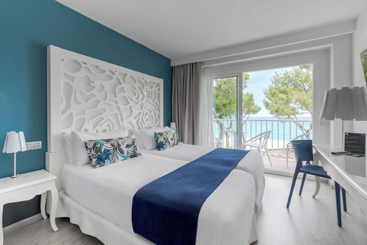 A hotel room with a large bed, a desk, and a view of the sea.