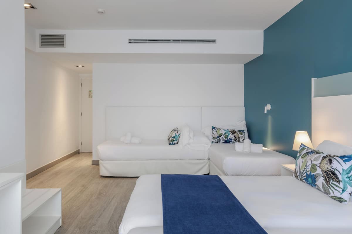 A modern hotel room with two beds, a blue blanket, and a white color scheme.