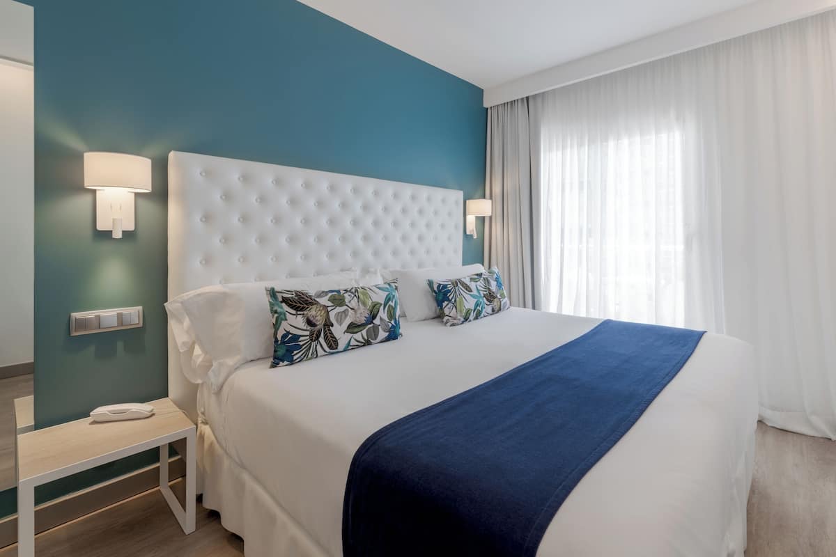 A hotel room with a large bed, a nightstand, and a wall-mounted lamp.
