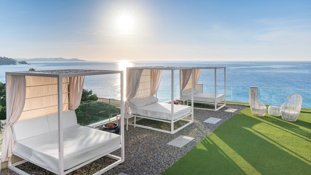 A balcony with two white beds, a small table, and two wicker chairs. - Hotel Planamar by Escampa Hotels (Castell-Platja d'Aro)