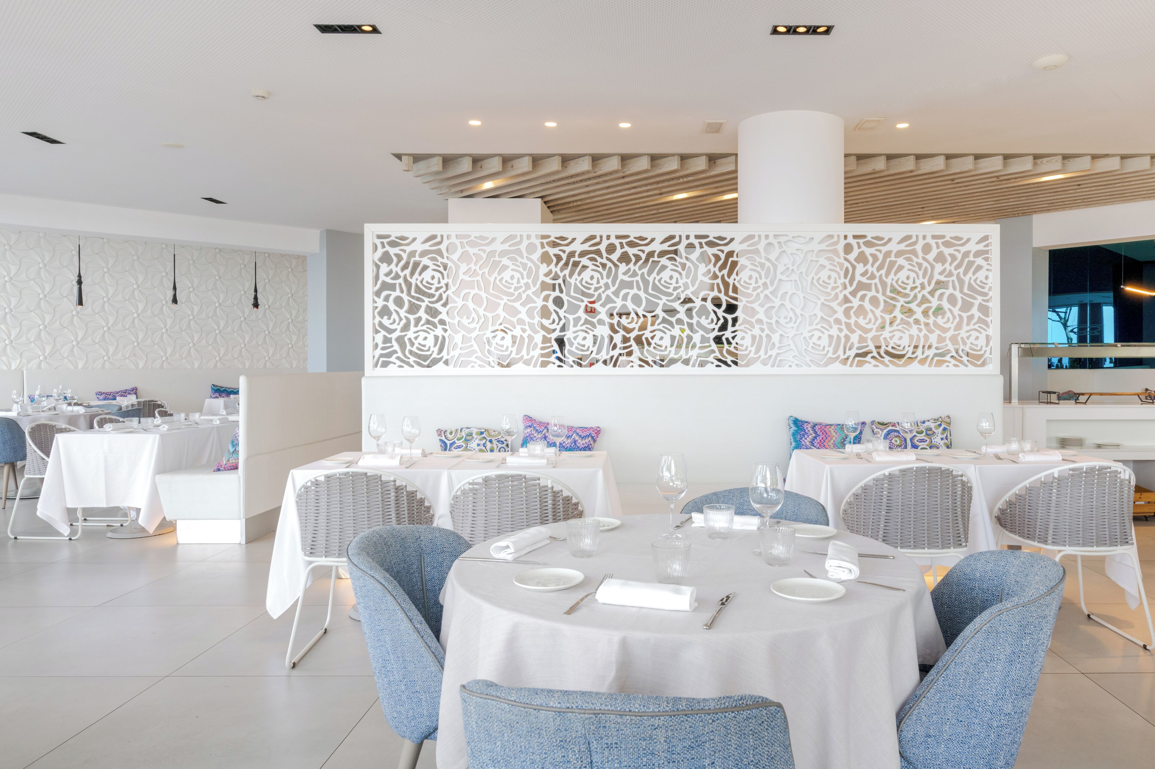 A modern dining area with round tables, blue upholstered chairs, and white tablecloths.