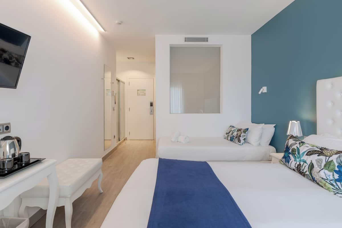 A modern hotel room with a large bed, a bedside table with a kettle, a small desk, and a mirror.