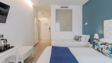 Una habitación de hotel moderna con una cama grande, una mesita de noche con hervidor, un escritorio pequeño y un espejo.