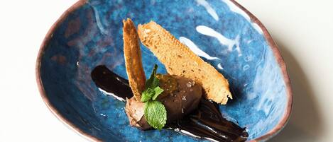 A blue ceramic bowl containing a dessert with a chocolate element, a piece of bread, and a mint leaf.
