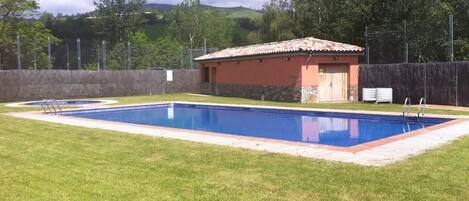 Una piscina rectangular con solárium empedrado, rodeada de césped cuidado.