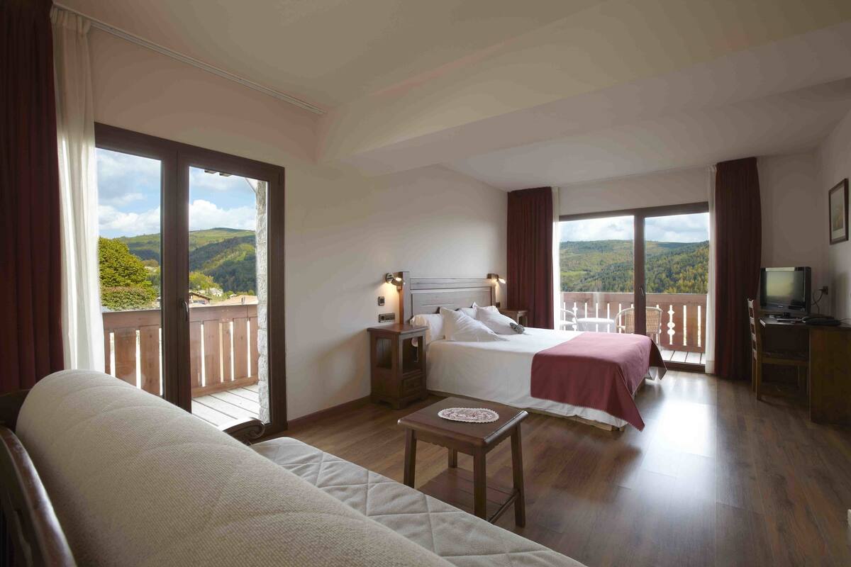A bedroom with a bed, a desk, and a view of the outdoors.
