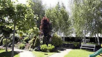 Un jardín ajardinado con un sendero, un banco y un tobogán verde.