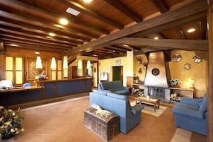 Un vestíbulo amplio con vigas de madera, una recepción, sofás y una chimenea.