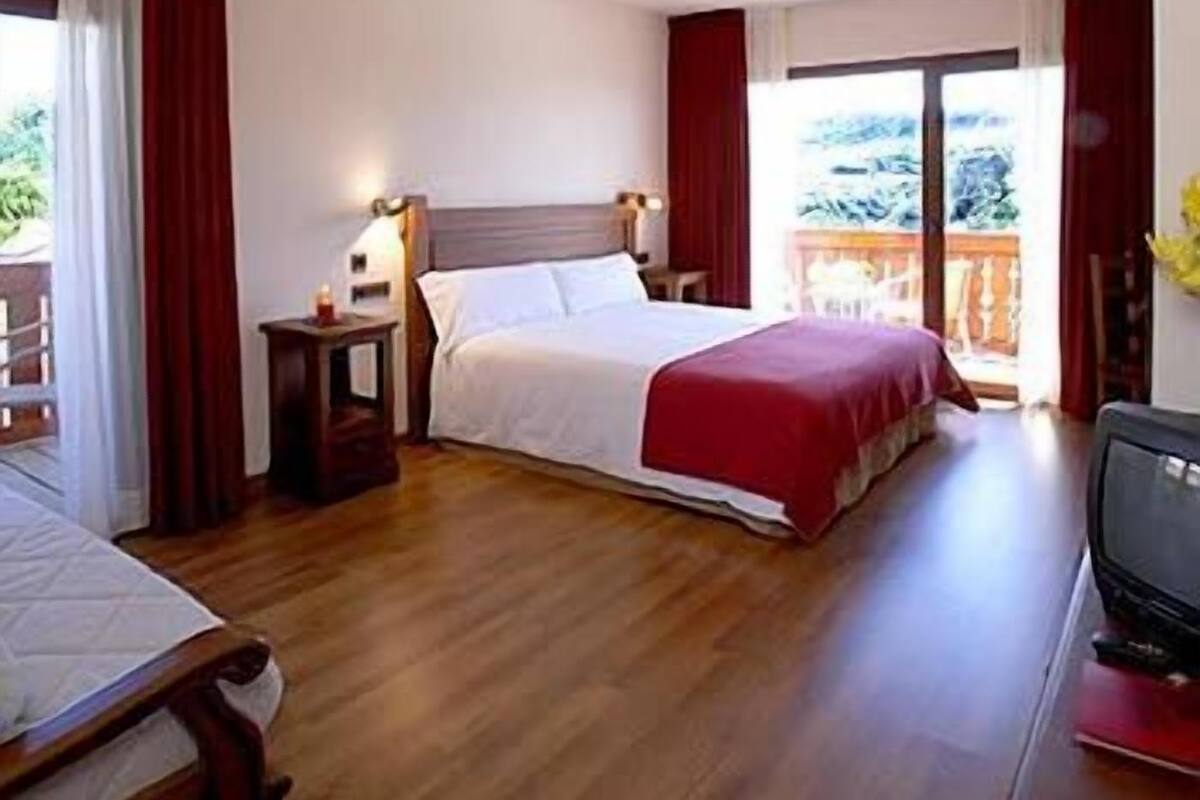 A hotel room with a bed, a nightstand, a TV, and a balcony with a view.