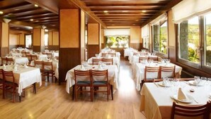 A restaurant with multiple tables set for dining, wooden beams on the ceiling, and large windows offering a view of the outdoors. - Calitxó (Mollo)
