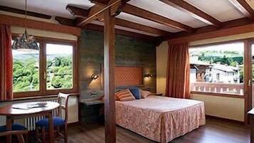 A bedroom with a bed, a desk, and a chair. There are windows with curtains, and a view of greenery outside.