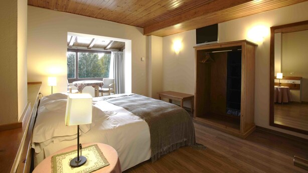 A bedroom with a wooden ceiling, a bed with a white comforter, a bedside table with a lamp, a wooden bench, a wardrobe, and a large mirror. - Calitxó (Mollo)