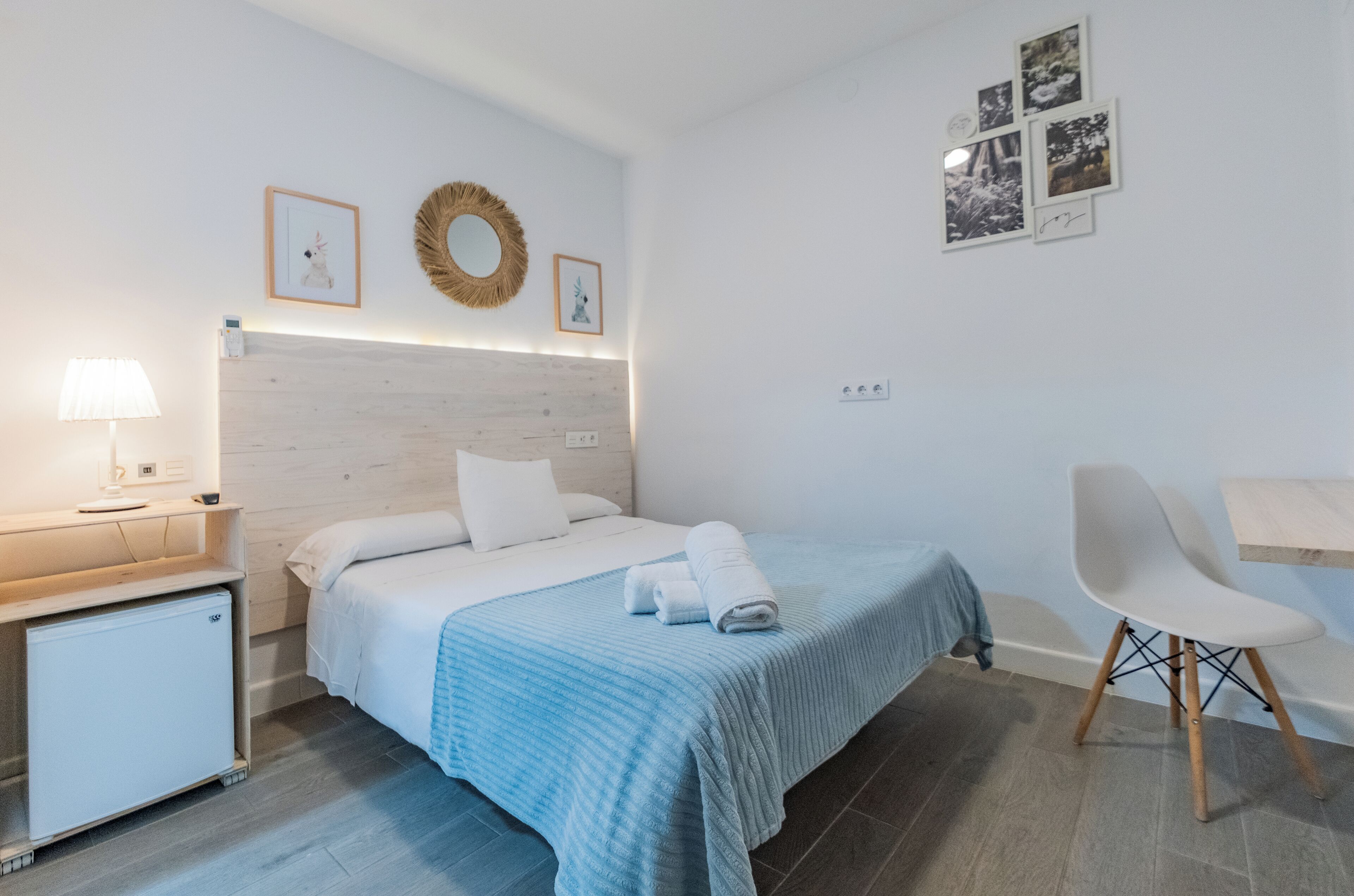 A hotel room with a bed, bedside table, lamp, and a small refrigerator.
