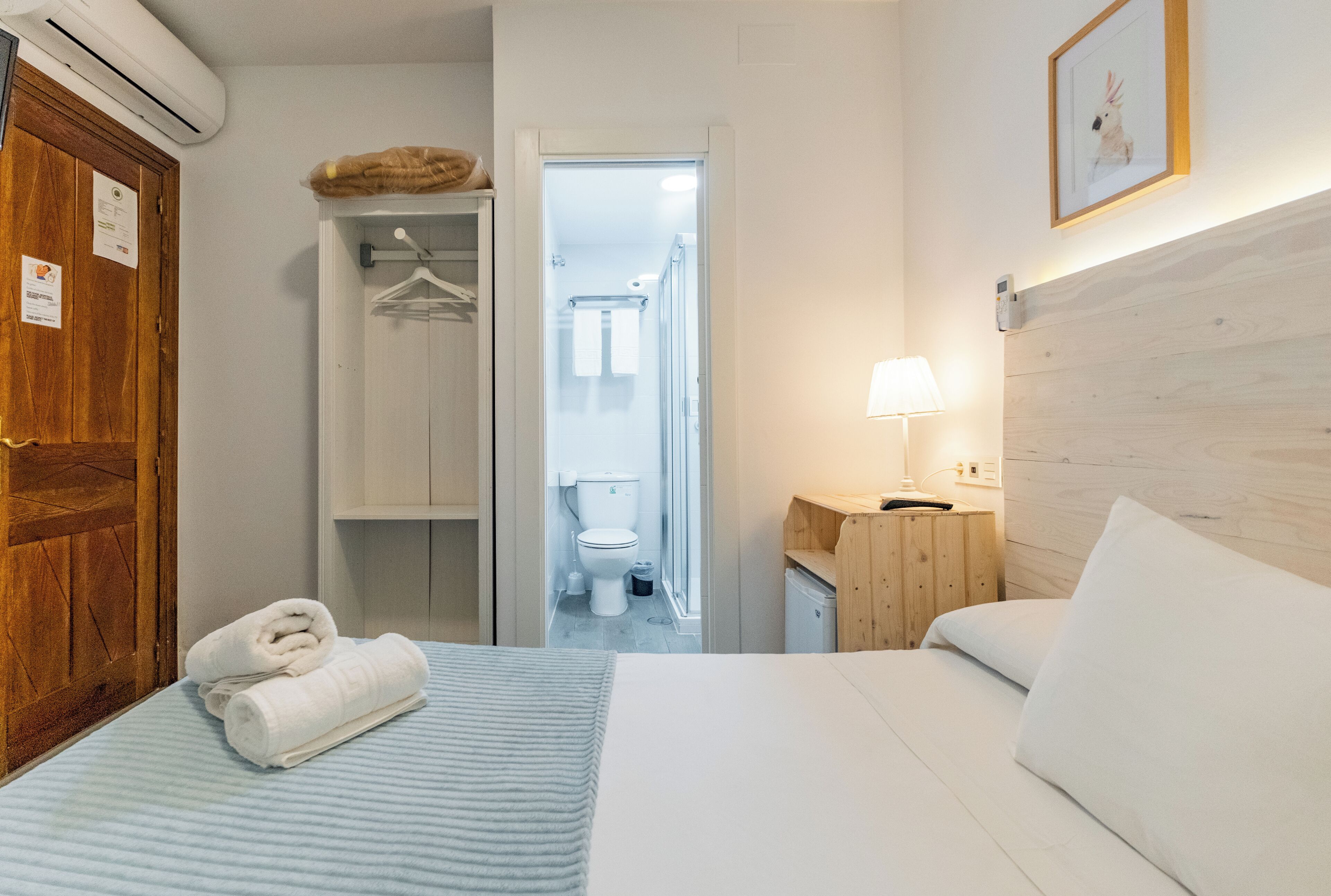 Habitación de hotel con cama, armario de madera, baño visible a través de una puerta abierta y un cuadro en la pared.