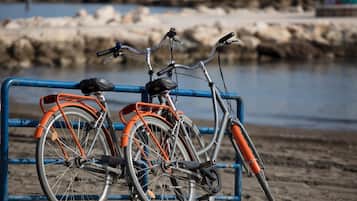 Dos bicicletas estacionadas frente a una barrera metálica azul, junto a una playa de arena con costa rocosa al fondo.