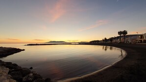 A coastal scene with calm waters, a sandy beach, and a row of buildings along the shore. - El Nogal Home - Hostel (Málaga)