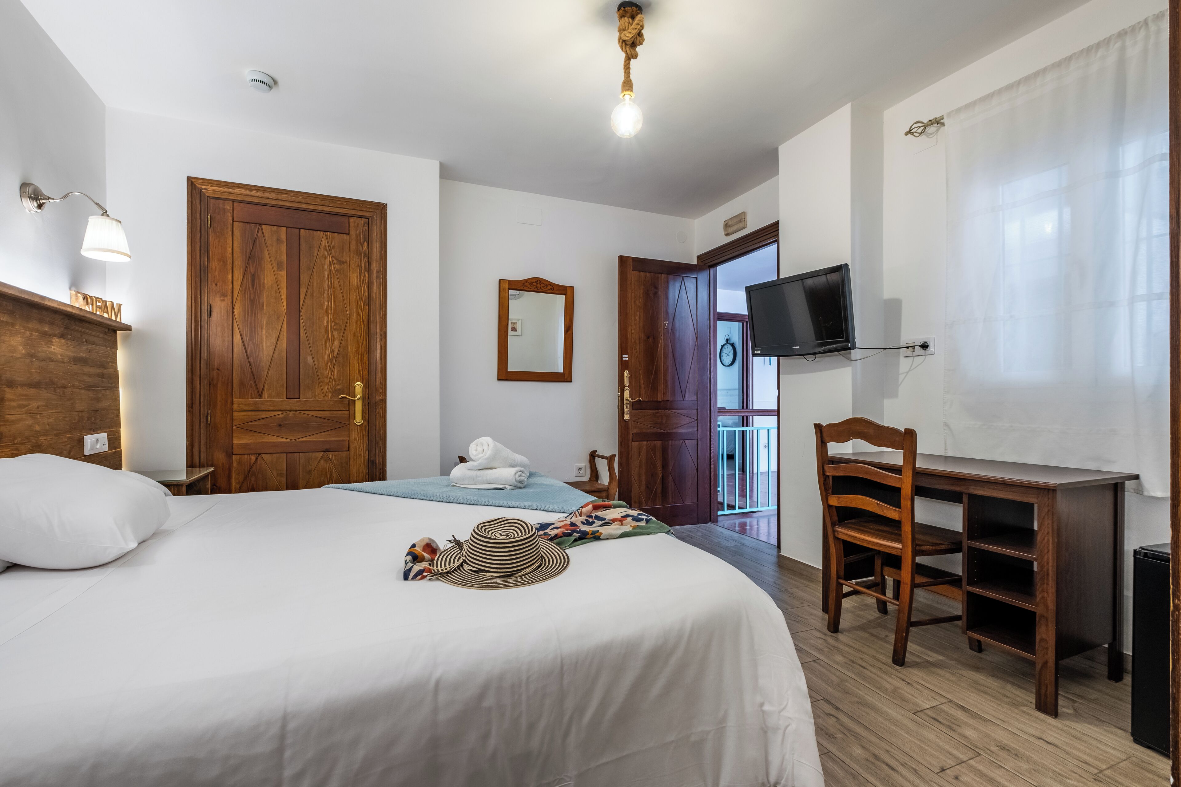 Une chambre d’hôtel équipée d’un lit, d’un bureau, d’une chaise, d’une télévision et d’une porte donnant sur un balcon.