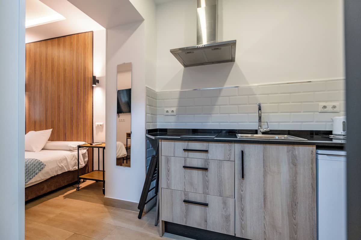 A compact kitchen with wooden cabinets, a stainless steel range hood, and a black countertop.