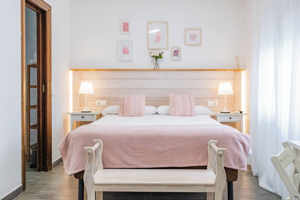 A neatly arranged bedroom with a bed, two bedside tables, a bench, and a wall with framed pictures.