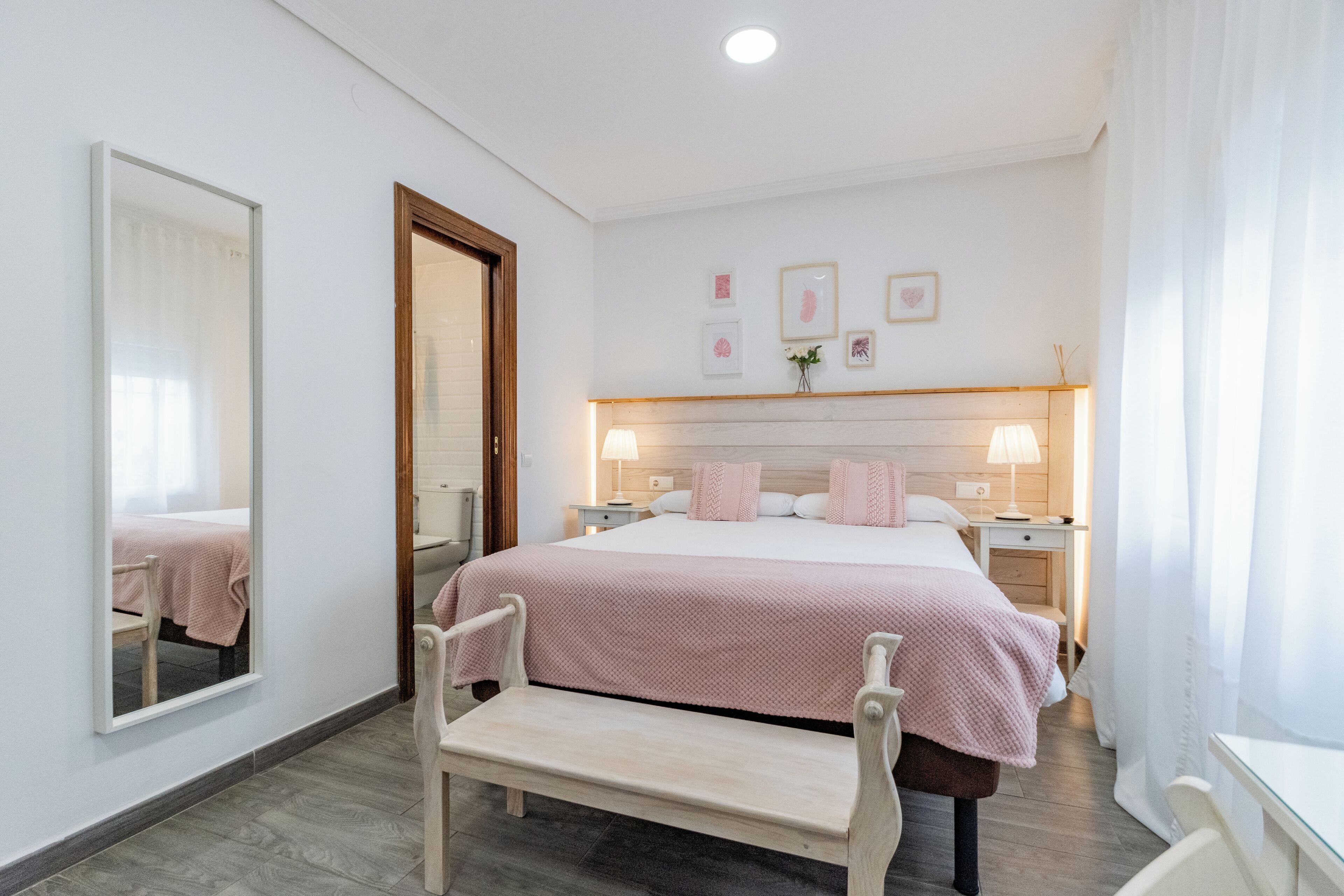 Un dormitorio con cama, mesitas de noche, un banco, un espejo y cuadros en la pared.