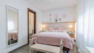 Un dormitorio con cama, mesitas de noche, un banco, un espejo y cuadros en la pared.