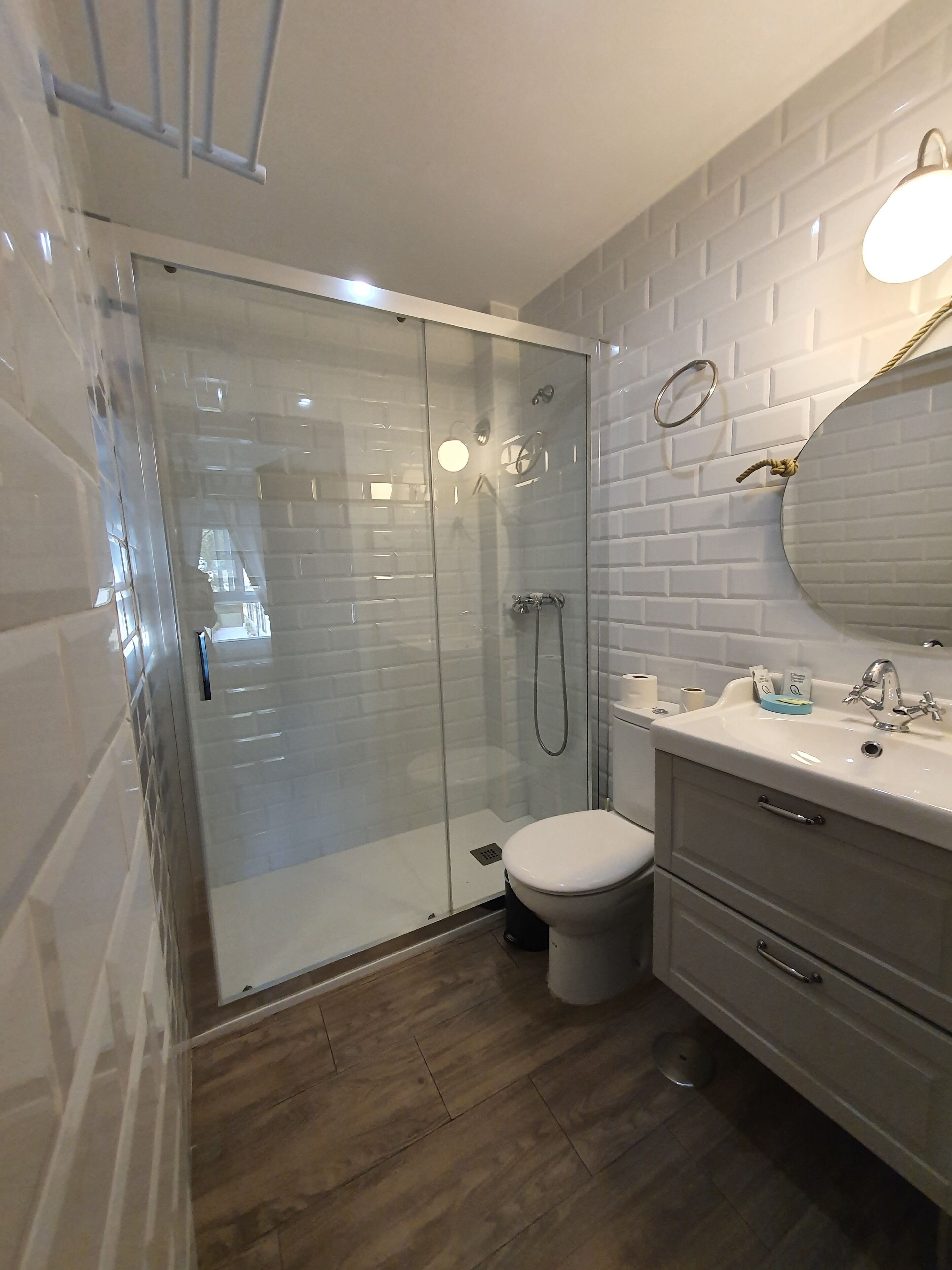 Un baño moderno con ducha envuelta en vidrio, inodoro blanco y tocador con espejo y lavamanos.