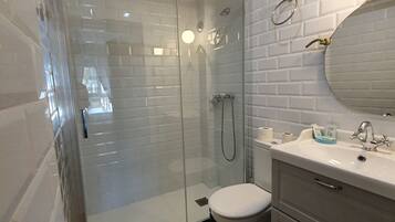 Un baño moderno con ducha envuelta en vidrio, inodoro blanco y tocador con espejo y lavamanos.