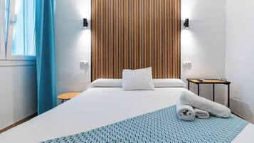 A hotel room with a large bed, a wooden panel wall, a small round table, and a blue patterned throw.
