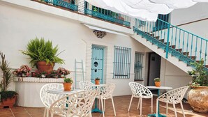A courtyard with white chairs and tables, potted plants, a blue door, and a turquoise staircase. - El Nogal Home - Hostel (Málaga)