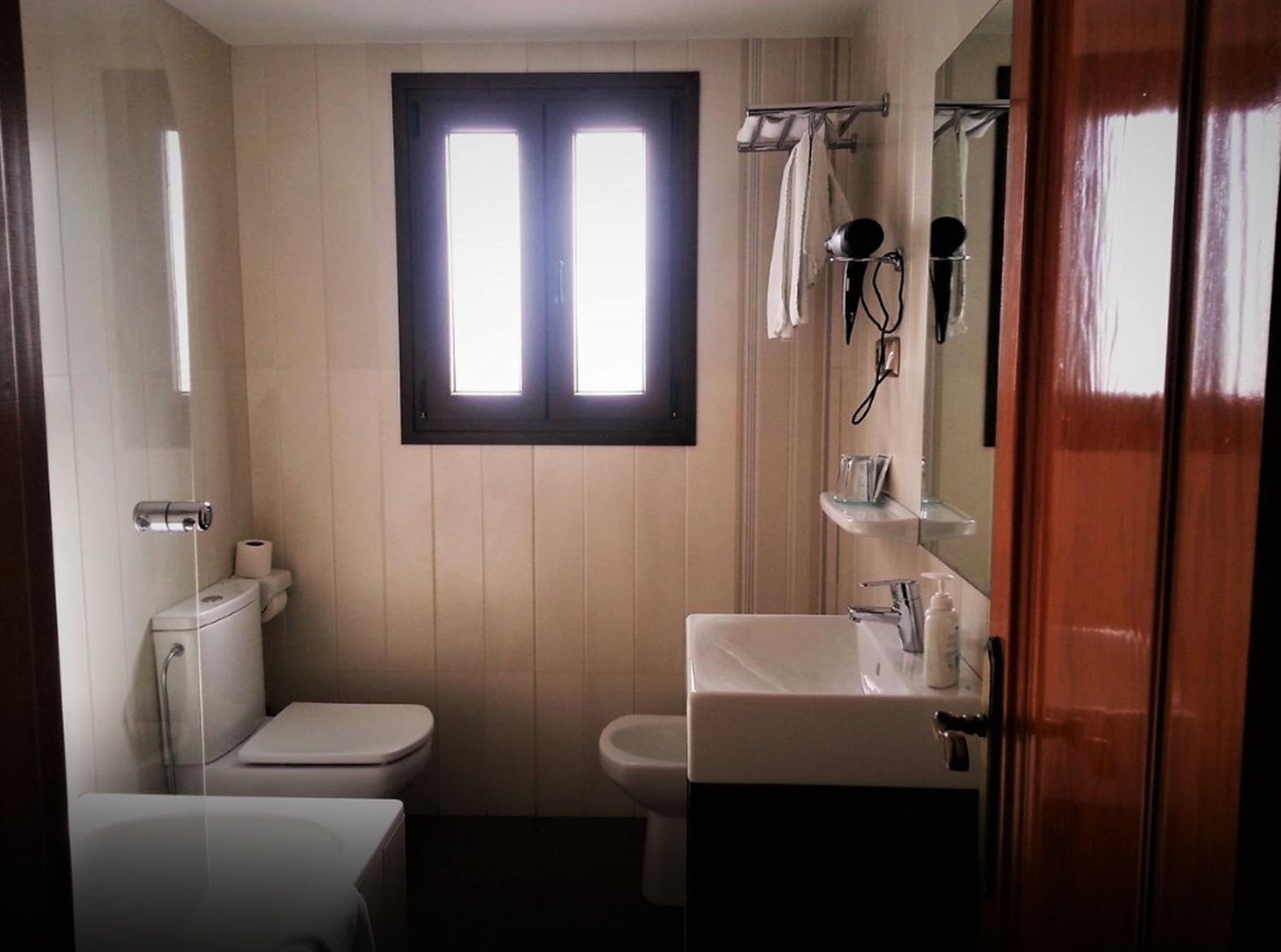 Une salle de bain équipée de toilettes, d’un bidet et d’un lavabo. Il y a une fenêtre au-dessus des toilettes et un miroir au-dessus du lavabo.