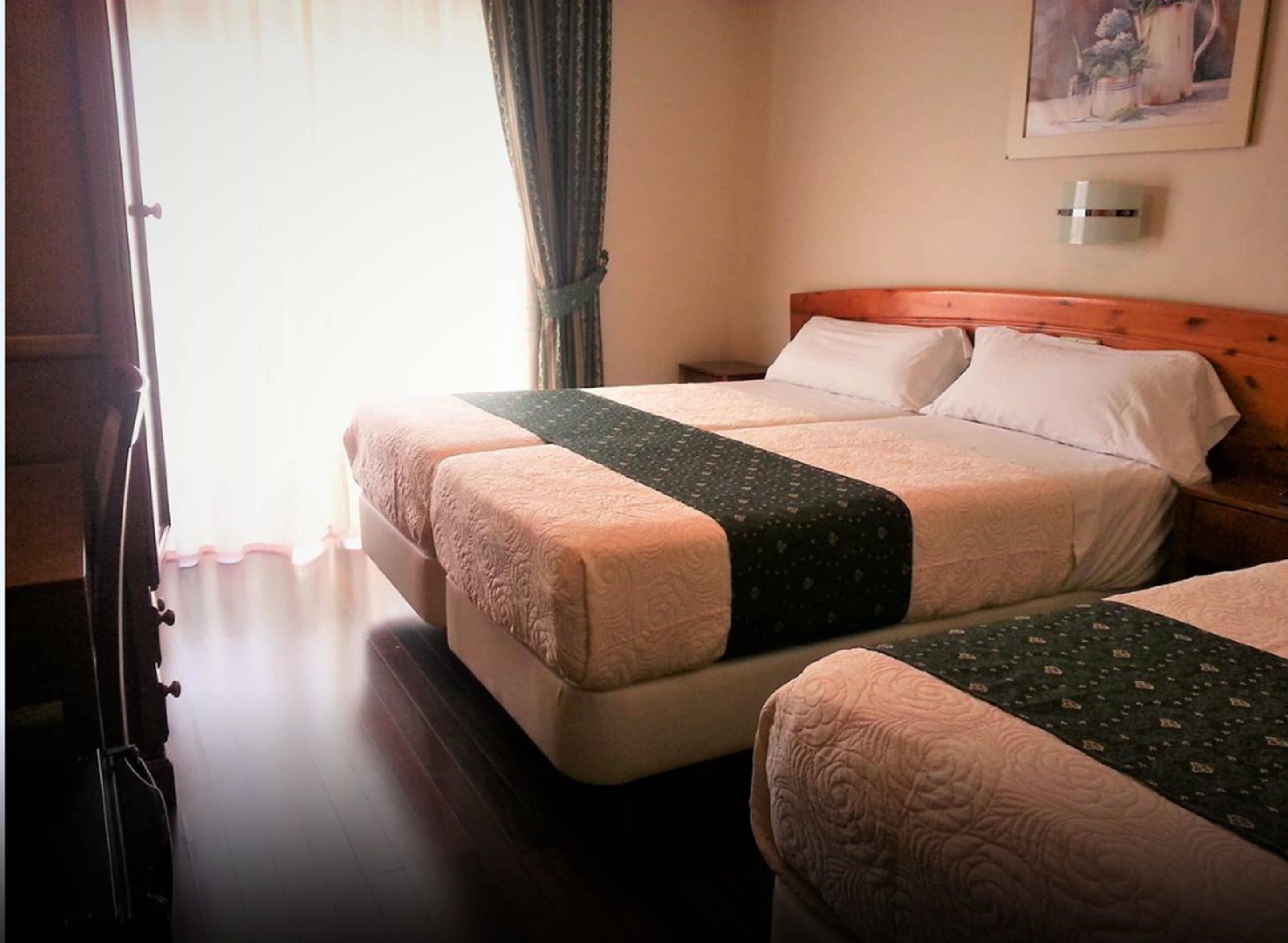 A hotel room with two beds, a wooden headboard, a painting on the wall, and a window with curtains.