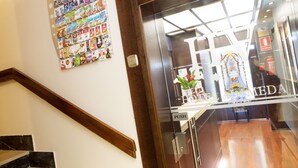Ein Hotel Eingang mit einer Holztreppe, einem Schwarzdbrett mit verschiedenen Anzeigen und einem Empfangstresen mit einem 'PUSH'-Hinweis.