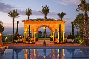 A pool area with a decorative archway, palm trees, and seating areas. - Hotel El Mirador (Alhaurin el Grande)
