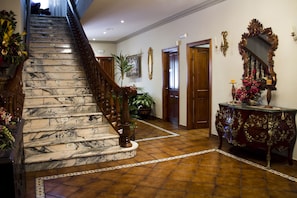 A grand staircase with marble steps and wooden railings, leading to a room with a large ornate mirror, a wooden console table, and potted plants. - Hotel El Mirador (Alhaurin el Grande)