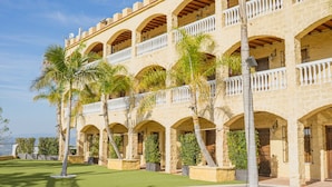 Un immeuble à plusieurs étages, orné d’une série d’arcades et de balcons, entouré de palmiers et d’une pelouse bien entretenue.