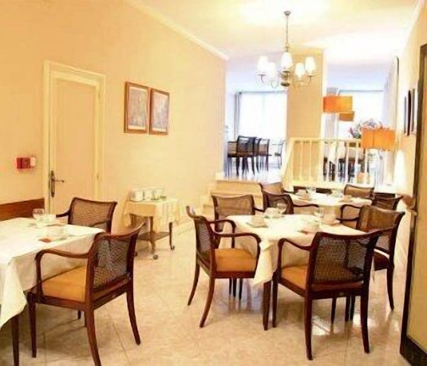 Un comedor con mesas y sillas redondas, una araña y cuadros en la pared.
