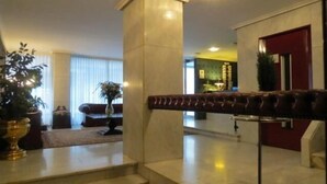 A spacious lobby with a red door, a leather bench, and a potted plant. - Hotel Monclús (Palencia)