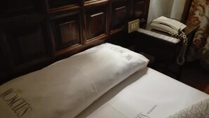 A hotel room with a neatly made bed, a telephone on a bedside table, and a wall with a patterned curtain. - Hotel Monclús (Palencia)