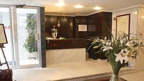 A modern lobby with a reception desk, a large vase of flowers, and a patterned rug. - Hotel Monclús (Palencia)
