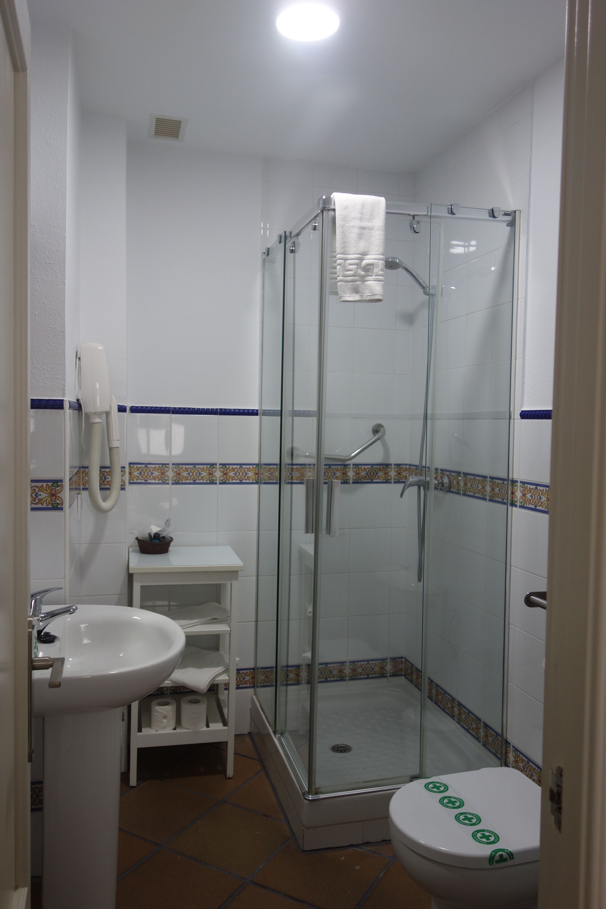A bathroom with a glass-enclosed shower, a white sink, and a toilet with a green sticker.