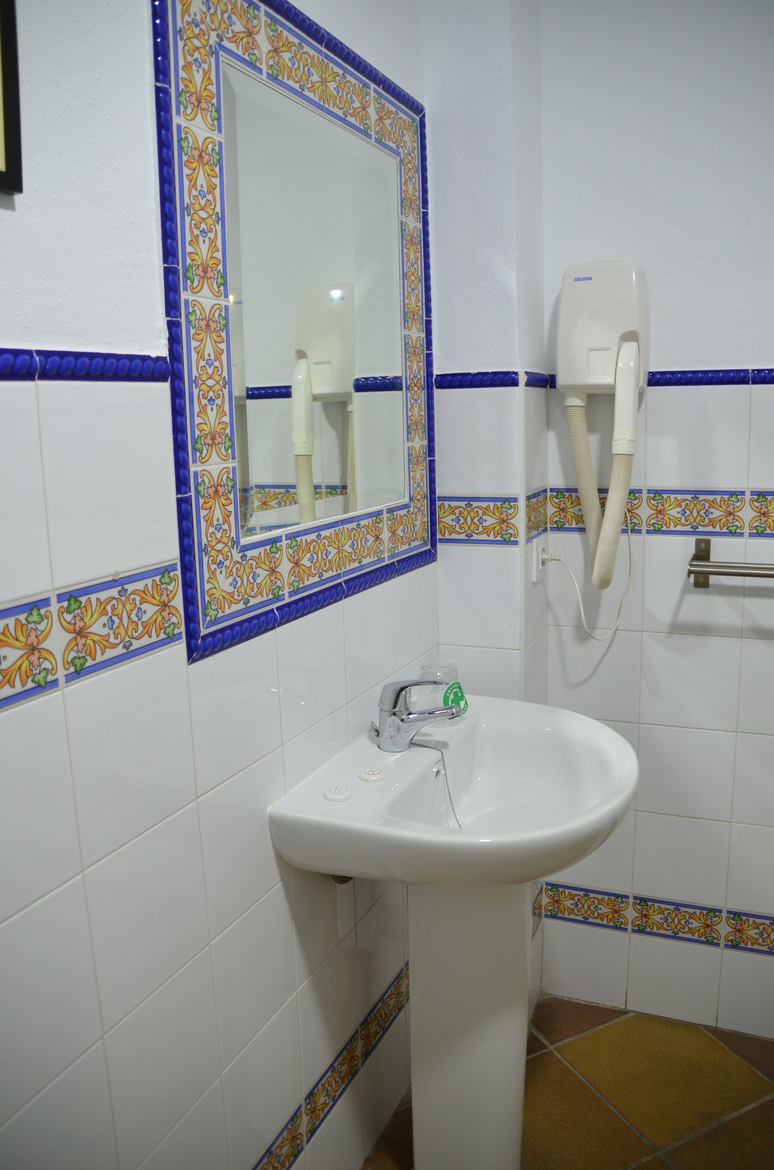 A bathroom with a white sink, a mirror with a decorative border, and a hand dryer.