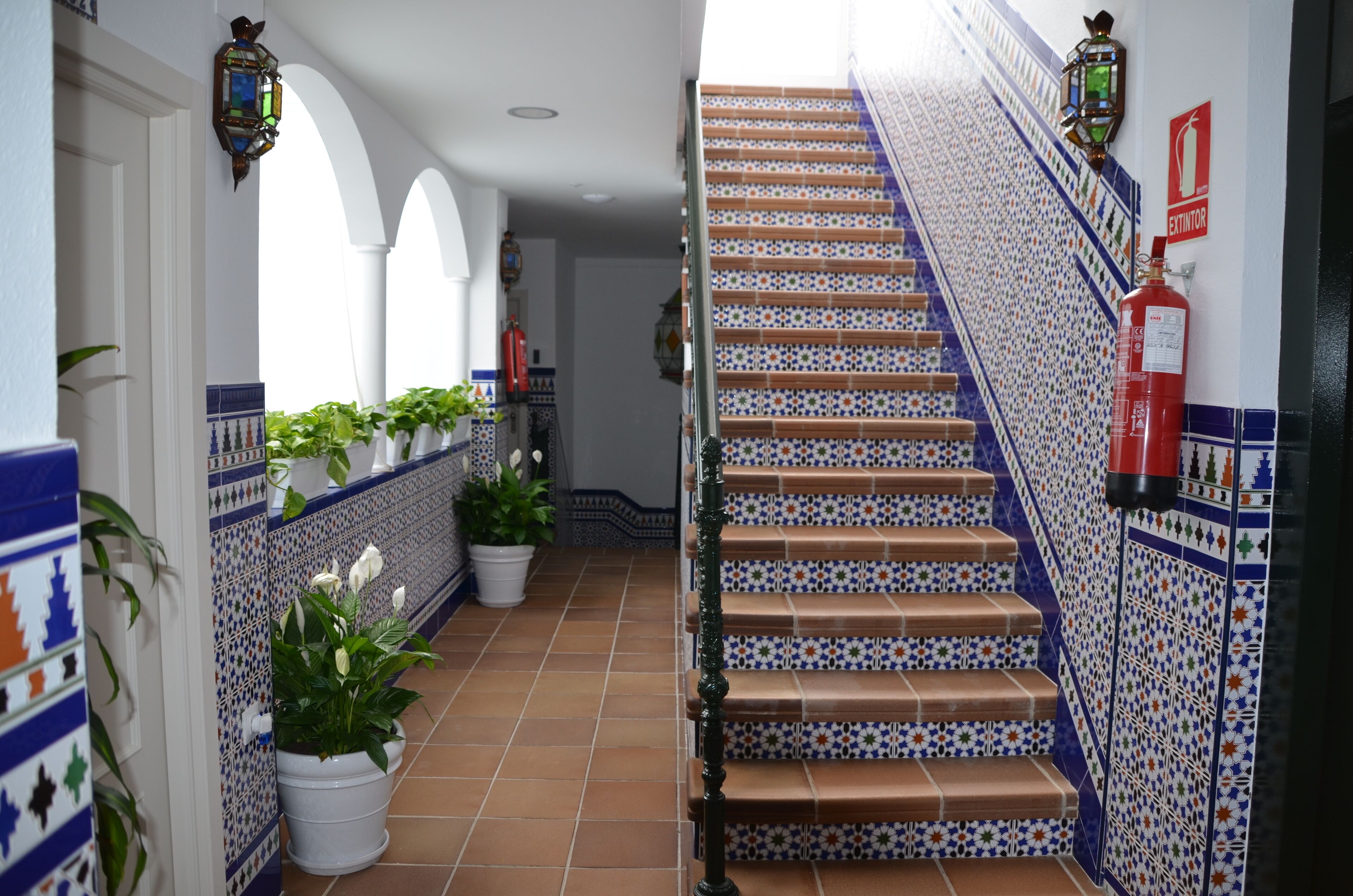 A hallway with a tiled staircase, potted plants, and a fire extinguisher.