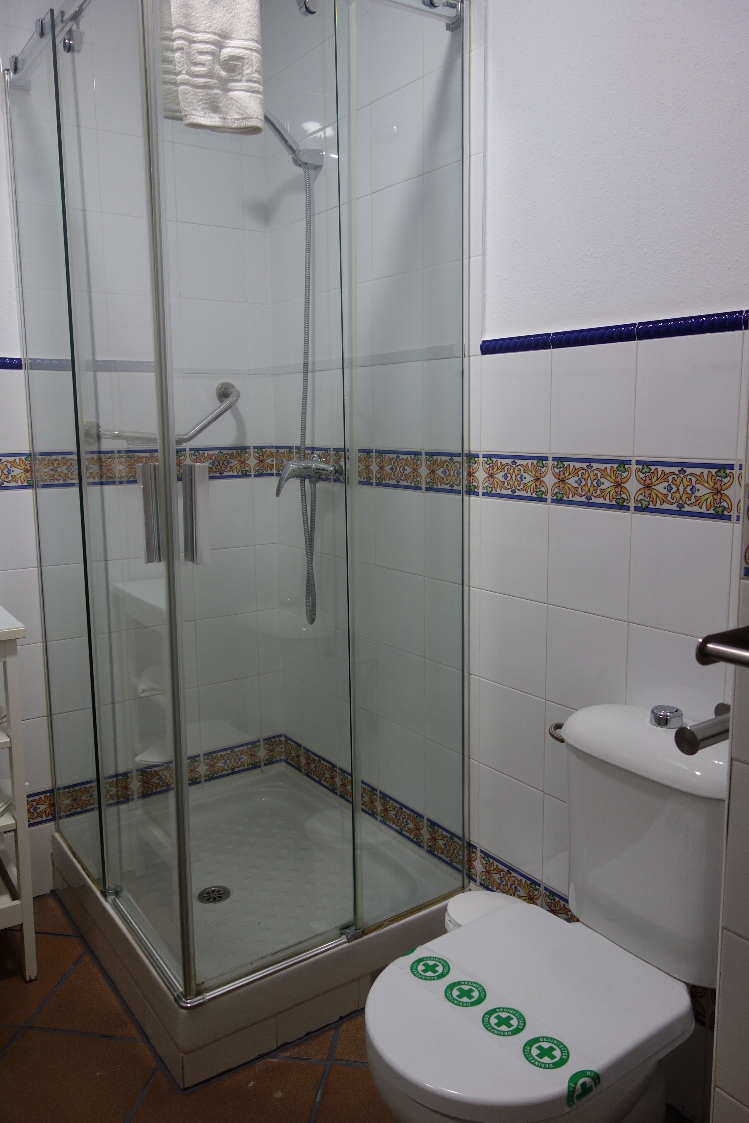 A bathroom with a glass-enclosed shower, a white toilet with green stickers, and a sink.