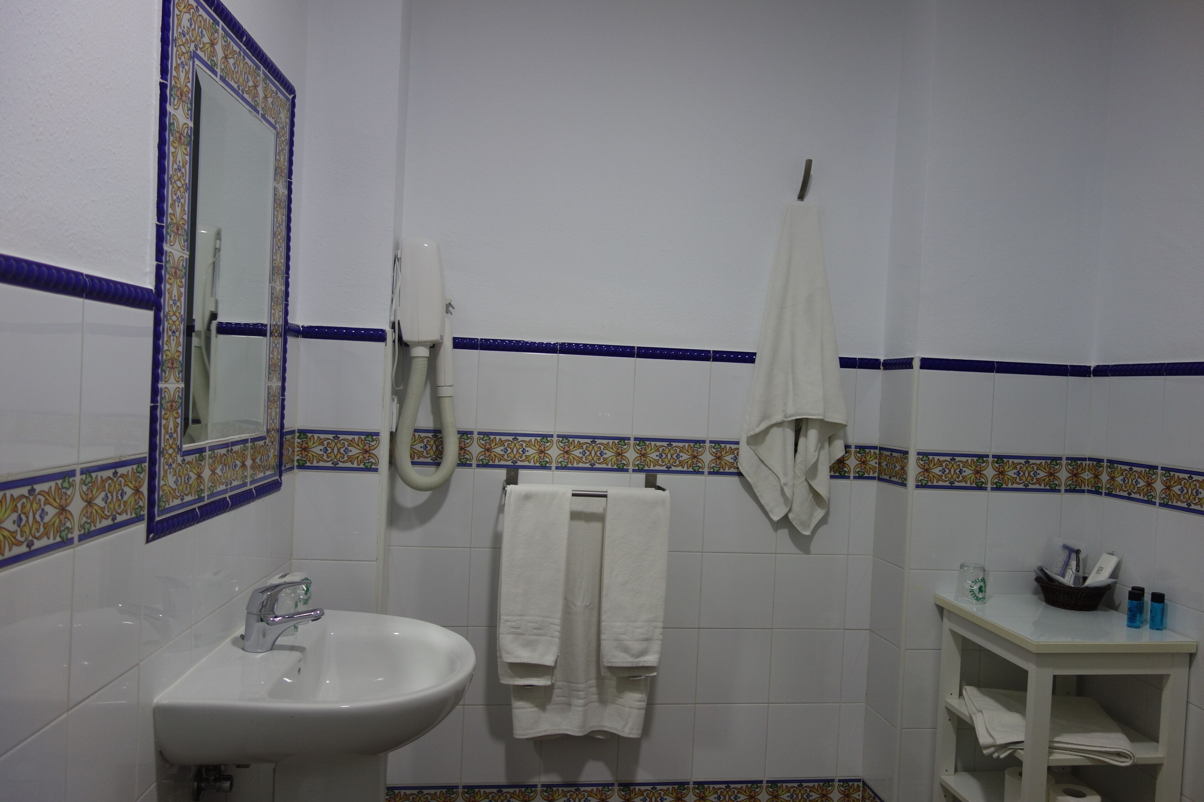 A bathroom with a white sink, a mirror, a towel rack, and a small shelf with toiletries.
